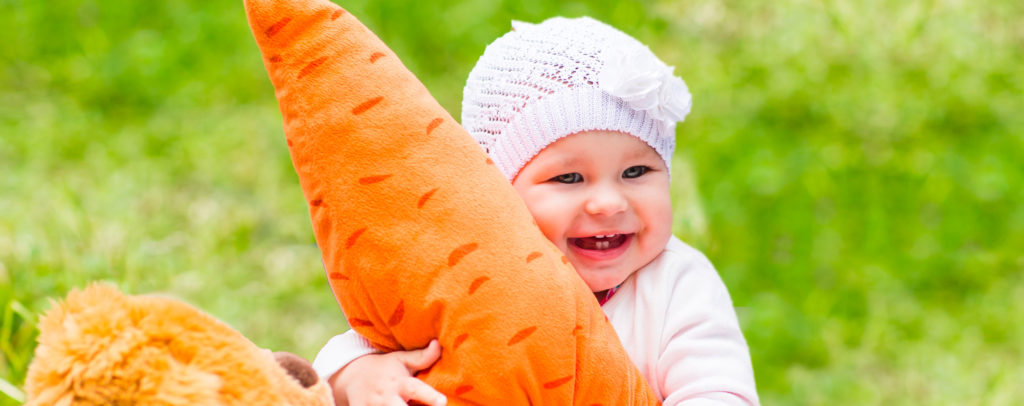 Un bébé avec une carotte en peluche pour évoquer l'alimentation du nourrisson